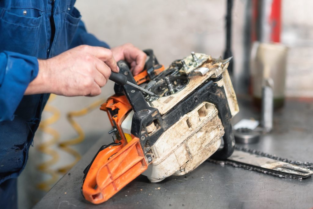 Mechanic repairing a chainsaw. Man repairing a chainsaw in workbench .